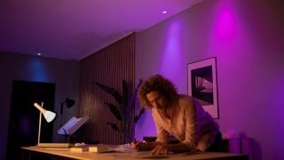 Las luces LED inteligentes Philips Hue crean un vibrante ambiente morado y rosa en la sala, mostrando una iluminación ambiental personalizable para las noches de cine y relajación en los hogares modernos.