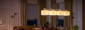 La moderna lámpara colgante LED con múltiples pantallas de tela ilumina una acogedora sala de estar, mostrando soluciones de iluminación doméstica energéticamente eficientes y elegantes para un confort de ambiente nocturno.