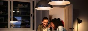 "Las modernas luces colgantes LED crean un ambiente cálido para dos mujeres que disfrutan de una conversación, mostrando soluciones de iluminación doméstica energéticamente eficientes".